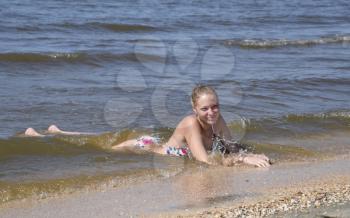 Blond girl in a bikini lying on the beach and the waves splash on it. Beautiful young woman in a colorful bikini on sea background.