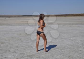 Girl standing on the dry bottom of a salt lake. Walk the dark-haired woman in a swimsuit on the bottom of a dry lake with salt and mud. The ancient dried-up lake.