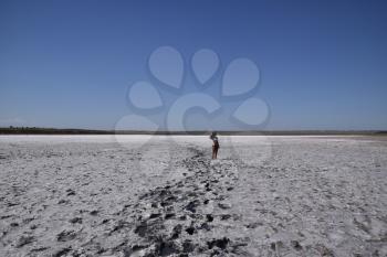 Girl standing on the dry bottom of a salt lake. Walk the dark-haired woman in a swimsuit on the bottom of a dry lake with salt and mud. The ancient dried-up lake.