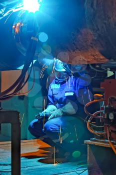 Welder resting during a break at work. Welding of the pipeline. Process of creation of welding connection by the special mobile machine. Worker sitting on a chair.