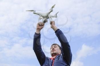 A man with a quadrocopter in his arms raised to the sky. A white drone is being prepared for the flight
