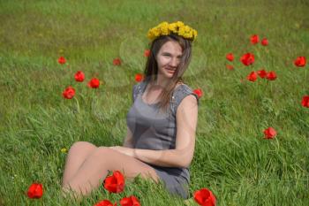 A girl with a wreath of dandelions on her head. Beautiful fairy young girl in a field among the flowers of tulips. Portrait of a girl on a background of red flowers and a green field. Field of tulips.