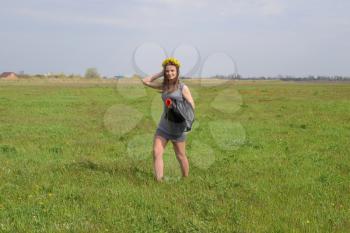 A girl with a wreath on her head from dandelions walks along the green field. Field of tulips.