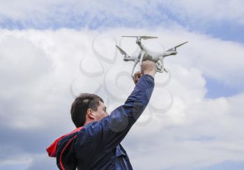 A man with a quadrocopter in his arms raised to the sky. A white drone is being prepared for the flight