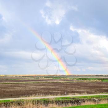 Rainbow, a view of the landscape in the field. Formation of the rainbow after the rain. Refraction of light and expansion in terms of spectra.