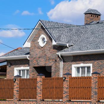 Asphalt shingle. Decorative bitumen shingles on the roof of a brick house. Fence made of corrugated metal