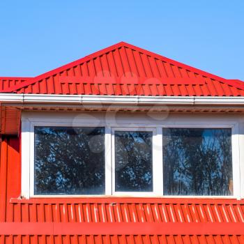 House with plastic windows and a red roof of corrugated sheet. Roofing of metal profile wavy shape on the house with plastic windows.