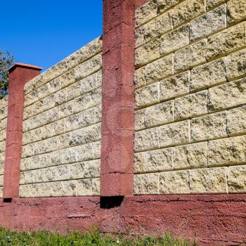 Fence made of bricks and decorative plaster. Yellow fence with red elements. High and beautiful fencing.