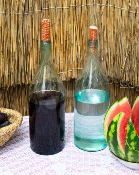 Bottles of wine and moonshine on the table. A basket with a plum and a watermelon as a snack. Traditional alcoholic drinks.