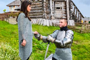 A knight in armor knelt before his lady heart. Knightly armor and weapon. Semi - antique photo.