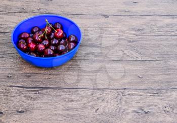 Berries of a sweet cherry on a wooden background in a plastic cup. Ripe red sweet cherry.