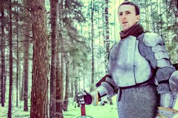 Knight in armor and with a sword in the middle of a winter forest. Vintage military uniform.