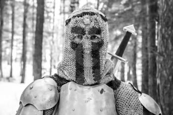 Knight in armor and with a sword in the middle of a winter forest. Vintage military uniform.