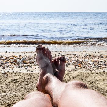 The legs of a man on a beach background. A man lies on an amatrace on the beach and is resting. Legs in the frame