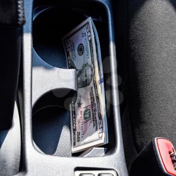 Several banknotes American dollars lie in the niche of the central console of the car. The money in the car.