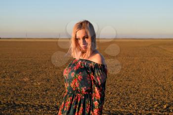Woman in a plowed field in a red-black dress on a sunset background