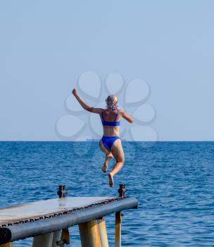 A beautiful girl in a blue bikini jumps from the pier into the water. Jumping in the sea.