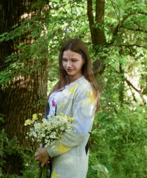 Young beautiful woman is standing in the forest with a bouquet of chamomiles.