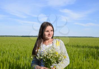 Young beautiful girl with a bouquet of chamomiles. A woman in a barley field.
