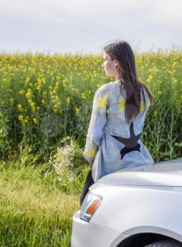 A girl with a bouquet of daisies sits on the hood of the car and looks into the distance
