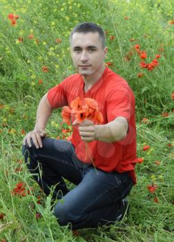 A young man in a red T-shirt is holding a bouquet of red poppies. The man is giving flowers. Poppy field.