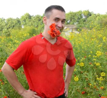 A young man in a red T-shirt is holding a bouquet of red poppies in his teeth. The man is joking. Poppy field.
