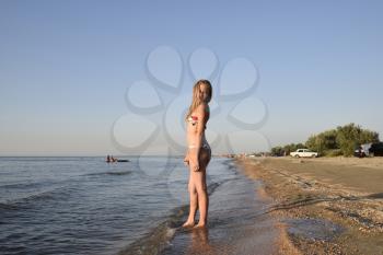 Blond girl in a bikini on the beach. Beautiful young woman in a colorful bikini on sea background.