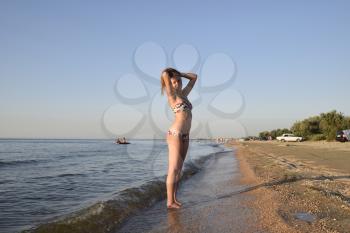 Blond girl in a bikini on the beach. Beautiful young woman in a colorful bikini on sea background.