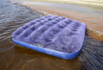 Blue inflatable mattress swimming in the pond. An inflatable mattress on the beach.