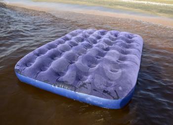 Blue inflatable mattress swimming in the pond. An inflatable mattress on the beach.