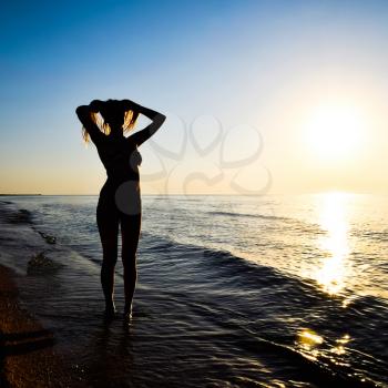Silhouette of a girl against the sunset by the sea. The dark silhouette against the sea sunset. Girl on the beach in the evening.