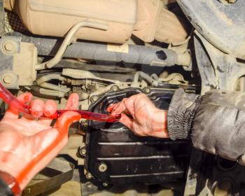 Oil change in automatic transmission. Filling the oil through the hose. Car maintenance station. Red gear oil. The hands of the car mechanic in oil.
