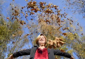 A woman throws up the autumn yellow leaves. Autumn in the park.