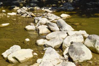 The mountain river. Shallow mountain river, water flows through the rocks. Rocks in the river water. Stones and layers of sedimentary rocks