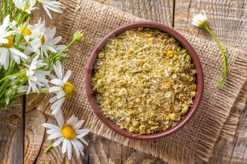 Dried and fresh chamomile flowers and leaves on wooden rustic background, alternative medicine
