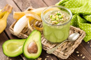Avocado and banana smoothie with oats with ingredients in glass jar on wooden background, healthy eating