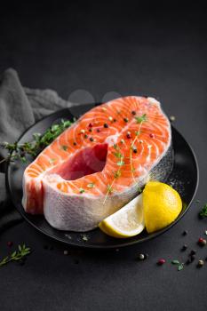 Salmon fish steak with lemon and thyme on black background