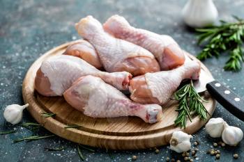 Raw uncooked chicken legs, drumsticks on wooden board, meat with ingredients for cooking