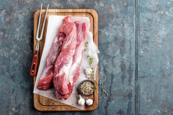 Fresh raw pork tenderloin on wooden cutting board on dark background