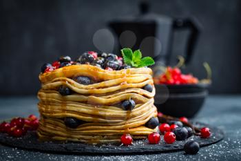 Pancakes with fresh berries and maple syrup on dark background, closeup