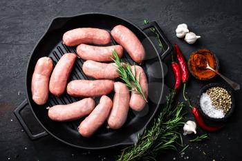 Fresh raw sausages on a cast-iron grill pan on a black background, top view