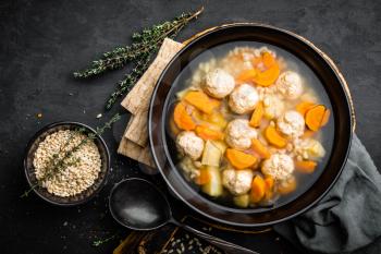 Fresh vegetable soup with meatballs and pearl barley in bowl on black background. Top view