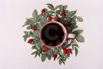 Cup of coffee on a white background in green leaves and red berries, flowers.Flat lay, top view