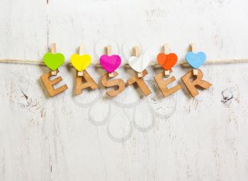 Easter word made of wooden letters with colored hearts clothespins on a white background old
