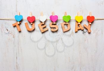 word Tuesday from wooden letters with colored clothespins on a white wooden background