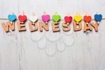 Wednesday word from wooden letters with colored clothespins on a white wooden background