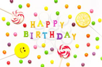 The phrase happy birthday, lollipops, candy smile on, are scattered around the colorful jelly beans on a white background.  Top view, flat