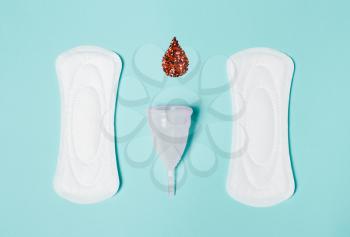 Pad, menstrual cup, tampon with a drop of blood on a blue background. The view is flat. Concept of critical days, menstruation
