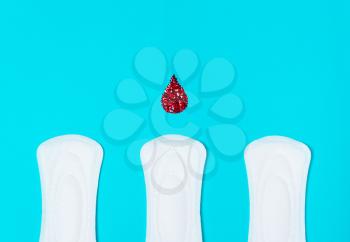 three menstrual pads with a drop of blood on a blue background. Concept of critical days,  cycle, menstruation