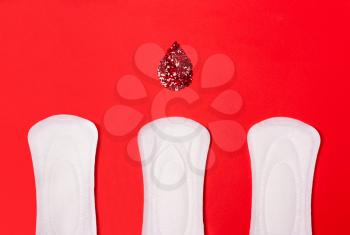 Three sanitary pads on a coral red background. The concept of critical days, menstruation, women's periodic cycle.
